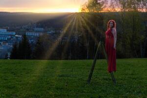 femme dans une rouge robe et une échelle dans une le coucher du soleil photo