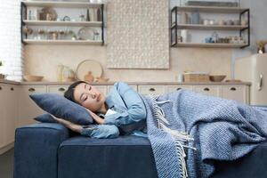 fermer photo de une Jeune magnifique asiatique femme en train de dormir à Accueil mensonge sur le canapé couvert avec une couverture, repos après travail pour dans le vivant pièce femme avec fermé yeux.