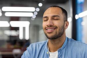 fermer photo de une calme et souriant Jeune arabe homme qui est dans le travail Bureau et repose et rêves avec le sien yeux fermé.