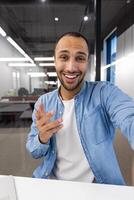 une homme est souriant et montrer du doigt à quelque chose. il est portant une bleu chemise et blanc chemise. le image a une décontractée et amical ambiance photo