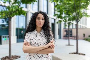 une femme dégage confiance avec sa bras franchi dans une moderne Urbain environnement, symbolisant responsabilisation et professionnalisme. photo