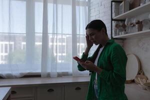 silhouette de une femme à Accueil dans le cuisine, une femme lit une triste message de le téléphone. photo