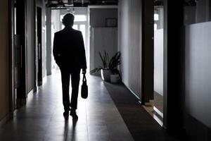 silhouette de une homme d'affaire dans plein hauteur, une homme à l'intérieur le Bureau des promenades le long de le couloir, entreprises, un employé dans une affaires costume. photo