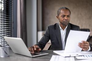 sérieux sur de soi homme d'affaire financier à l'intérieur Bureau à lieu de travail vérification documents, rapports et contrats. Sénior homme dans affaires costume travail sur formalités administratives, comptable avec comptes. photo