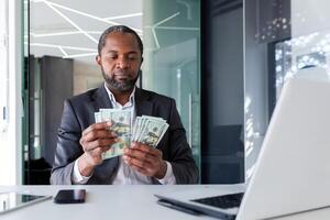 africain américain Jeune homme d'affaire séance à le bureau dans le Bureau et compte argent billets de banque. photo