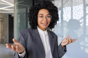 fermer portrait de un Afro-américain femme d'affaires ,séance dans une costume dans le Bureau à une bureau ,et parlant à le caméra sur une appel. photo