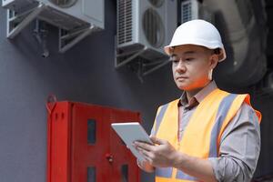 sérieux asiatique Jeune Masculin contremaître, construction inspecteur, ingénieur permanent près bâtiment et usine à l'extérieur et en utilisant tablette dans concentration. photo