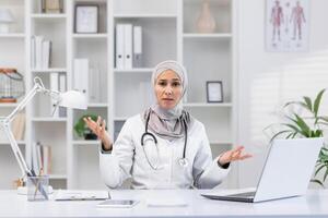 une femelle soins de santé professionnel dans une hijab apparaît frustré et confus, faire des gestes à sa portable dans une moderne Bureau paramètre. photo