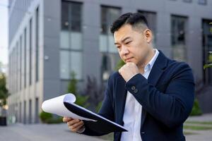 professionnel Masculin exécutif dans une costume concentré sur en train de lire et en cours d'analyse formalités administratives avec une réfléchi expression en plein air. photo