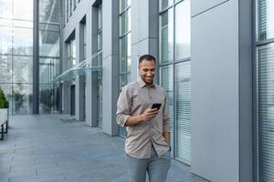 content africain américain homme d'affaire à la recherche à téléphone intelligent filtrer, homme dans chemise à l'extérieur moderne Bureau bâtiment reçu bien nouvelles de gagner et Succès en ligne, patron célébrer financier triomphe photo