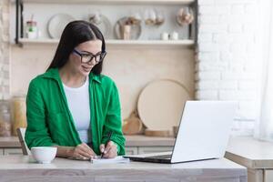 une Jeune femelle étudiant études en ligne à Accueil de une ordinateur portable, écoute à le conférence, écrit photo