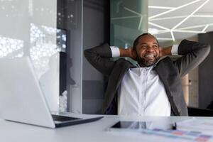 bien terminé homme d'affaire avec succès terminé le travail, repose dans le Bureau rêveusement et pensivement, le homme jette le sien mains derrière le sien tête et visualise le futur victoires et réalisation. photo