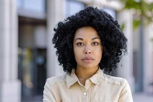 fermer portrait de Jeune sérieux en pensant femme à l'extérieur Bureau bâtiment, affaires femme avec frisé cheveux à la recherche à caméra. photo