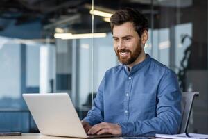 sur de soi Masculin professionnel avec une sourire travail sur une portable dans une contemporain Bureau environnement. photo