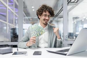 joyeux homme d'affaire fête financier Succès à lieu de travail avec en espèces dans main, exsudant confiance et réussite dans une moderne bureau. photo