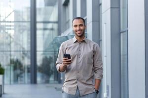 portrait de africain américain homme d'affaire, homme en portant téléphone souriant et à la recherche à caméra, Bureau ouvrier dans chemise à l'extérieur moderne Bureau bâtiment sur le déjeuner Pause photo