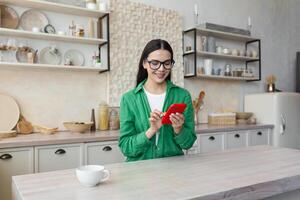 magnifique femme dans des lunettes et vert chemise en utilisant rouge mobile téléphone à Accueil photo