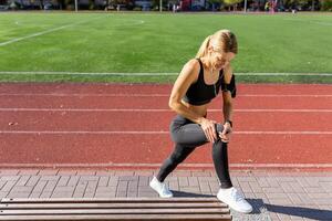 une en forme femme pauses à Regardez à sa aptitude traqueur pendant une faire des exercices session sur une ensoleillé Piste champ. photo