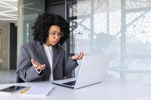 africain américain Jeune affaires femme parlant dans le Bureau sur une appel sur une ordinateur portable, lancement en haut sa mains dans frustration et déception. photo