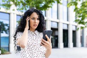 triste déçu femme reçu en ligne notification avec mal nouvelles sur sa téléphone, femme d'affaires en marchant à l'extérieur Bureau bâtiment, en utilisant application sur téléphone intelligent, en train de lire social médias insatisfait. photo