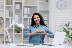 professionnel hispanique femme à Accueil Bureau fabrication cœur geste, exprimer l'amour et passion pour sa emploi. photo