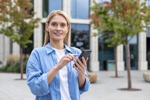 une Jeune adulte femelle des stands en plein air, concentré sur sa téléphone intelligent, avec moderne bâtiments dans le Contexte. le image capture une commun scène de connectivité et Urbain mode de vie. photo