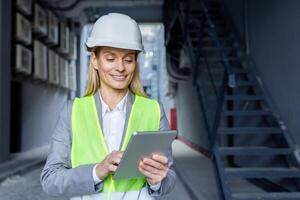 une souriant femelle ingénieur dans une difficile chapeau et sécurité gilet occupé avec une tablette sur une construction placer. photo