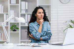 pensif latina femme d'affaires dans Accueil Bureau paramètre, dépeindre détermination et professionnalisme tandis que à travail. photo