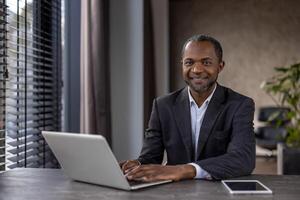 sur de soi et de bonne humeur africain américain exécutif travail à une élégant bureau, à la recherche à caméra avec une agréable sourire. photo