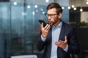 Sénior mature patron en colère en criant parlant sur téléphone, homme d'affaire dans affaires costume à l'intérieur Bureau près la fenêtre. photo