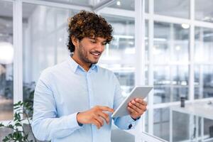 une souriant Jeune musulman homme, homme d'affaire, étudiant, designer permanent dans le Bureau et en utilisant une tablette. photo