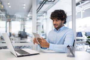 une homme habillé dans une bleu chemise engage avec une tablette à le sien ordonné poste de travail dans une brillant, contemporain Bureau paramètre. photo