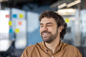 une joyeux âge moyen homme avec frisé cheveux souriant légèrement dans une décontractée travail environnement. il apparaît contenu et à faciliter, suggérant une confortable et positif Bureau atmosphère. photo