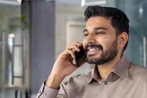 souriant Jeune homme engagé dans une téléphone conversation tandis que dans une moderne bureau. cette image capture le sien confiance et agréable comportement dans une professionnel environnement. photo