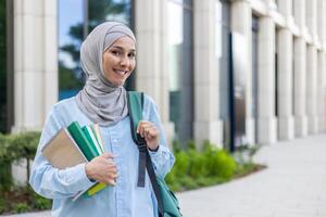 un élégant Jeune musulman femme dans hijab porter livres, Heureusement en marchant dans une affaires district, reflétant Urbain professionnel vie. photo