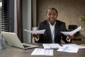 furieux arabe Masculin séance à espace de travail surchargé avec formalités administratives et à la recherche à caméra avec fronça les sourcils les sourcils. barbu homme en essayant à organiser les documents sur presse-papiers avec foiré information. photo