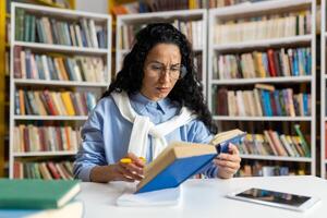 une dévoué étudiant absorbé dans en train de lire une livre entouré par une vaste collection de Littérature dans une bien approvisionné bibliothèque. photo