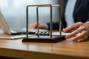 mature homme d'affaire dans une costume interagit avec une de newton berceau sur le sien bureau, symbolisant décision fabrication et se concentrer. photo