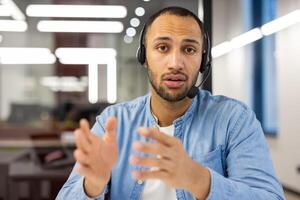 concentré Masculin client un service représentant portant une casque, engagé dans un actif discussion dans une moderne Bureau paramètre. photo