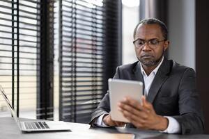 une homme dans une costume est en utilisant une tablette ordinateur. il est concentré sur le écran et il est fonctionnement. concept de productivité et concentration photo