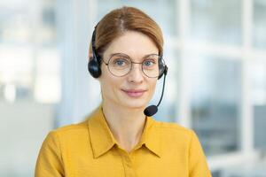 portrait de réussi souriant affaires femme avec casque téléphone, mature expérimenté ouvrier souriant et à la recherche à caméra, appel en ligne réunion, en ligne client soutien service. photo