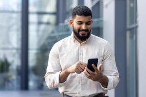 professionnel homme dans décontractée chemise en utilisant téléphone intelligent à l'extérieur moderne Bureau photo