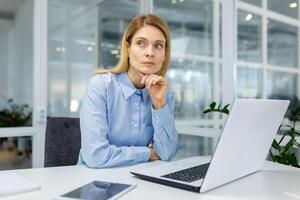 professionnel femme d'affaires Profond dans pensée tandis que travail à sa moderne Bureau bureau avec une ordinateur portable, tablette, et téléphone intelligent. photo