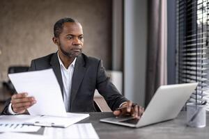 sérieux sur de soi homme d'affaire financier à l'intérieur Bureau à lieu de travail vérification documents, rapports et contrats. Sénior homme dans affaires costume travail sur formalités administratives, comptable avec comptes. photo