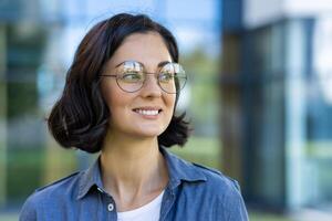 une de bonne humeur femelle étudiant jouit une ensoleillé journée sur Campus, portant des lunettes et une décontractée denim chemise. sa sourire reflète confiance et bonheur dans un éducatif paramètre. photo