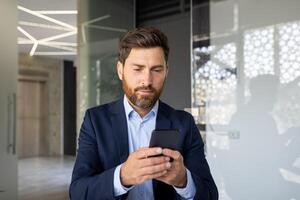 fermer photo de une Jeune sérieux Masculin homme d'affaire qui est dans une moderne Bureau et les usages une mobile téléphone.