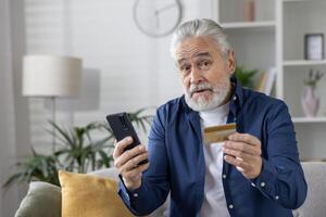 personnes âgées Masculin avec crédit carte et téléphone, potentiel victime de en ligne fraude dans une confortable Accueil paramètre. photo