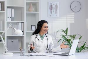 latino femelle médecin engageant dans une appel conversation avec une patient dans une moderne clinique Bureau paramètre. photo