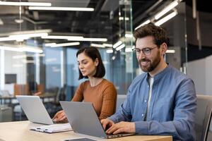 adulte couple dans décontractée vêtements travail avec des ordinateurs et à la recherche à écrans tandis que en utilisant clavier. couple de pigistes visite partagé Bureau zone pour création productif atmosphère en dehors de maison. photo