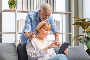 Sénior couple dans vivant chambre, femme et une homme en utilisant téléphone intelligent parlant sur appel, content famille concepts photo